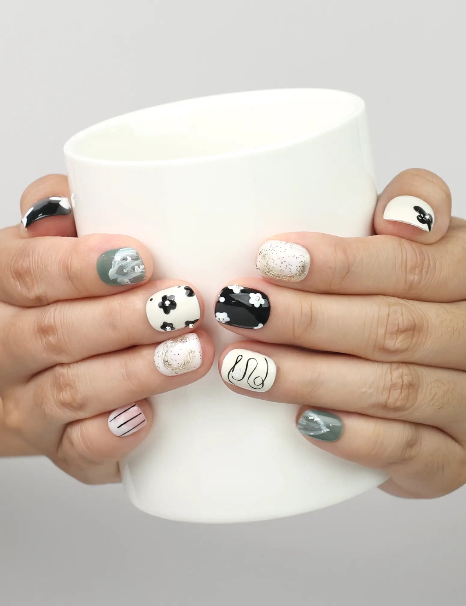 Model holding a cup while wearing Naillover Inky Blossoms handmade press on nails with black, white, and green floral abstract design.