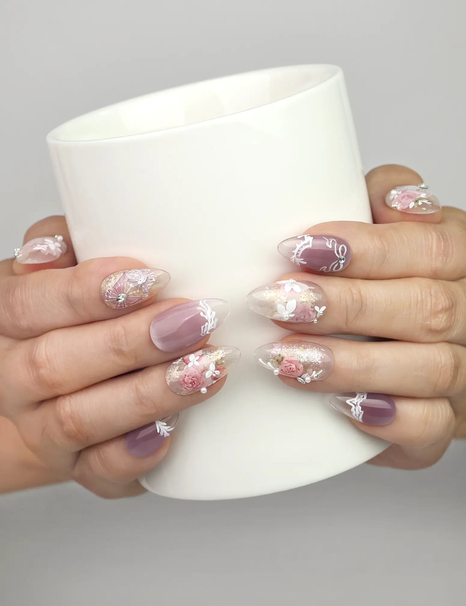Hand holding a cup wearing Naillover Lavender Floral Dream handmade press on nails in lilac and white with roses and butterflies.