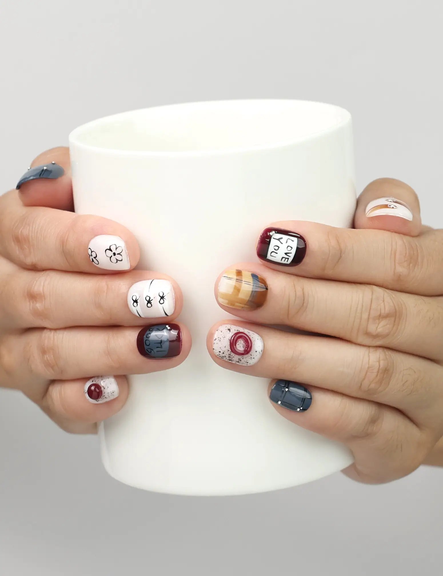 Model holding a cup while wearing Naillover Love Notes handmade Singapore press on nails with contrasting tones and floral details.