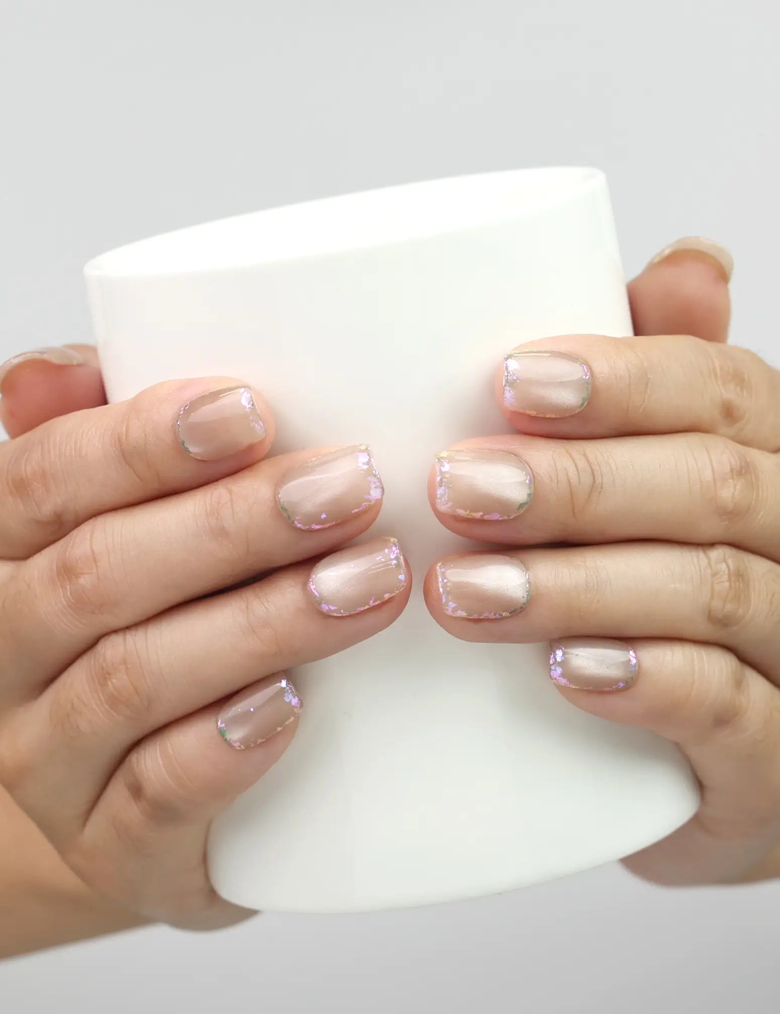 Model holding a cup while showcasing Naillover Lucent Blooms handmade Singapore press on nails with floral motifs.