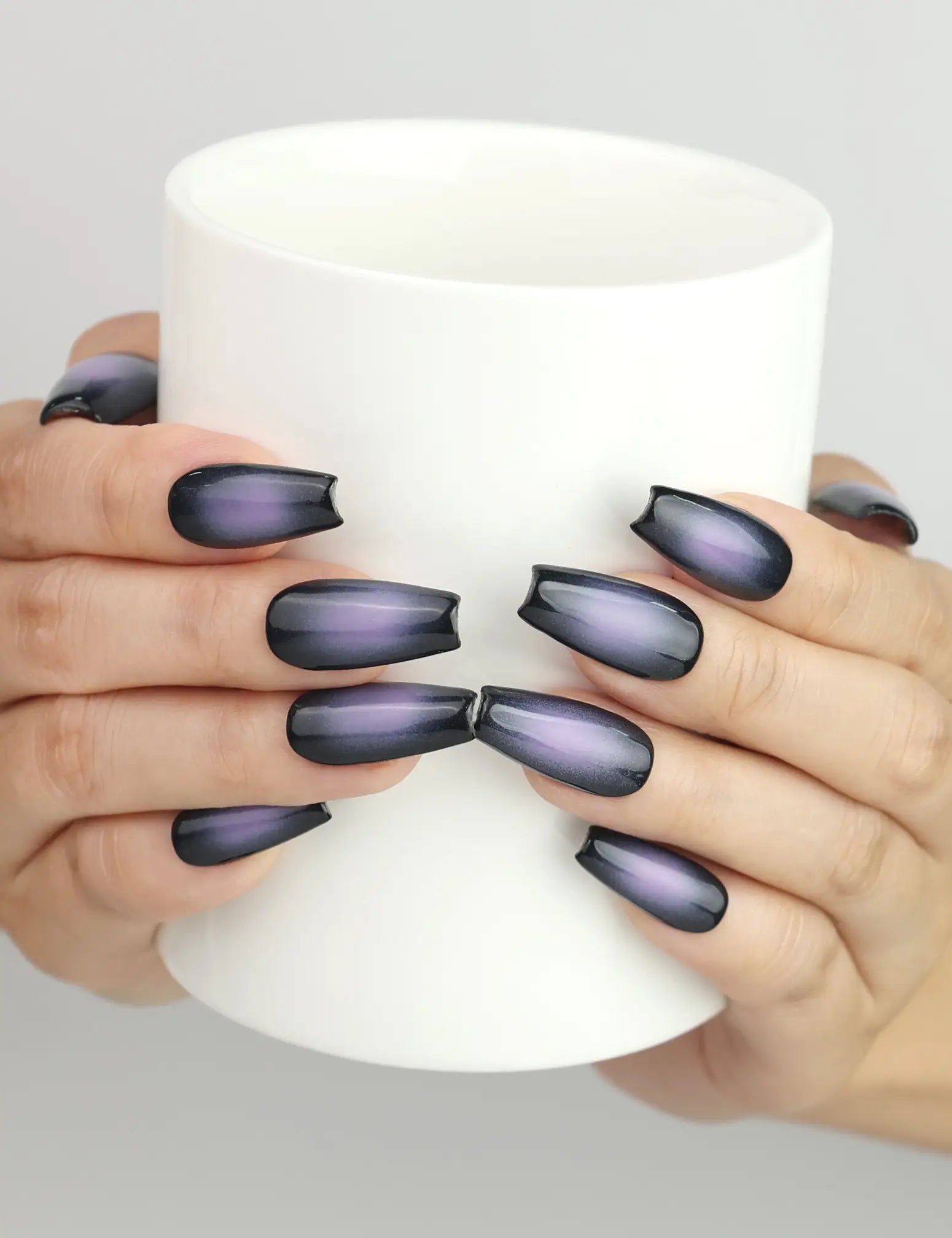 Hand holding cup with Naillover Lunar Eclipse press on nails, stylish black to purple ombre gradient set