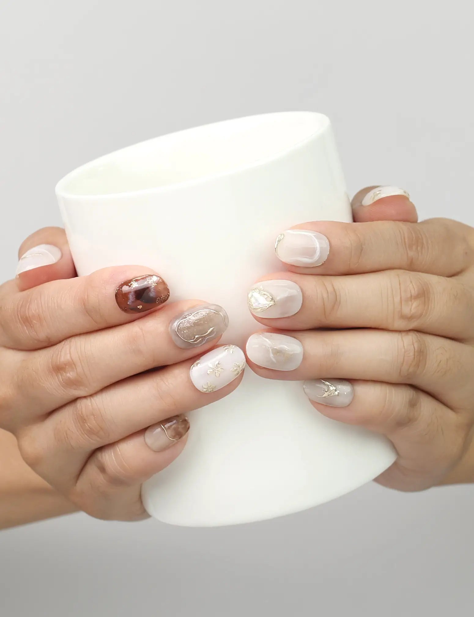 Model holding a cup while showing Naillover Marble Blossom handmade press on nails with white and brown marble finish.