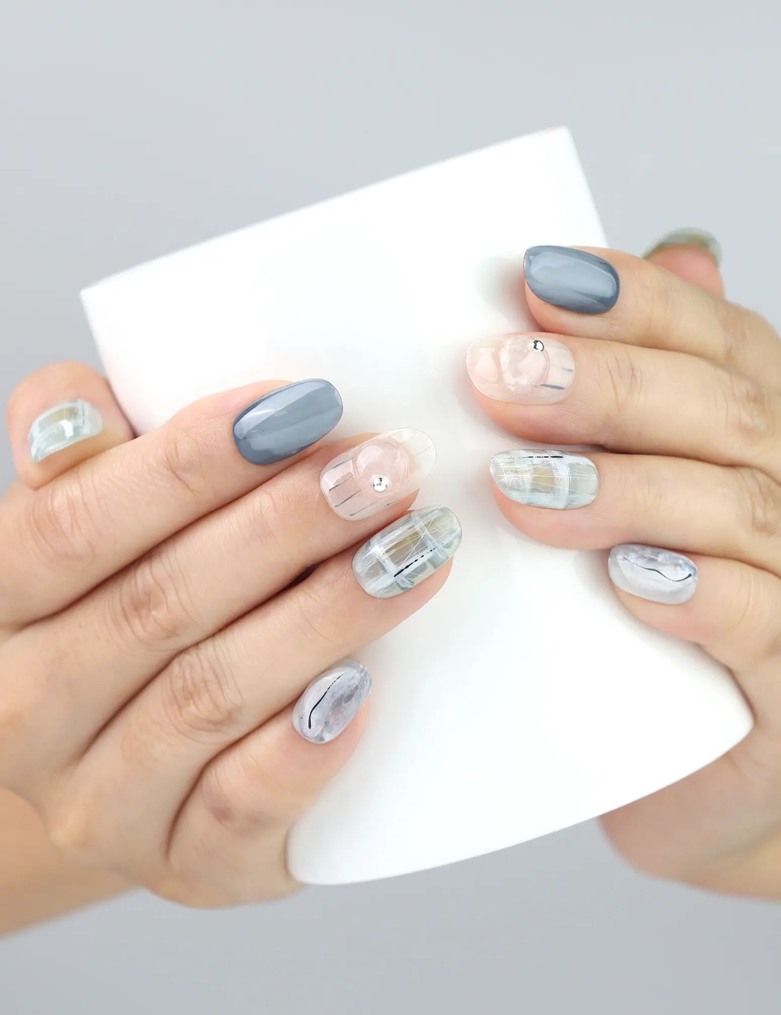 Hand holding a ceramic cup with Misty Grid press on nails from Naillover, featuring white and grey squared design.