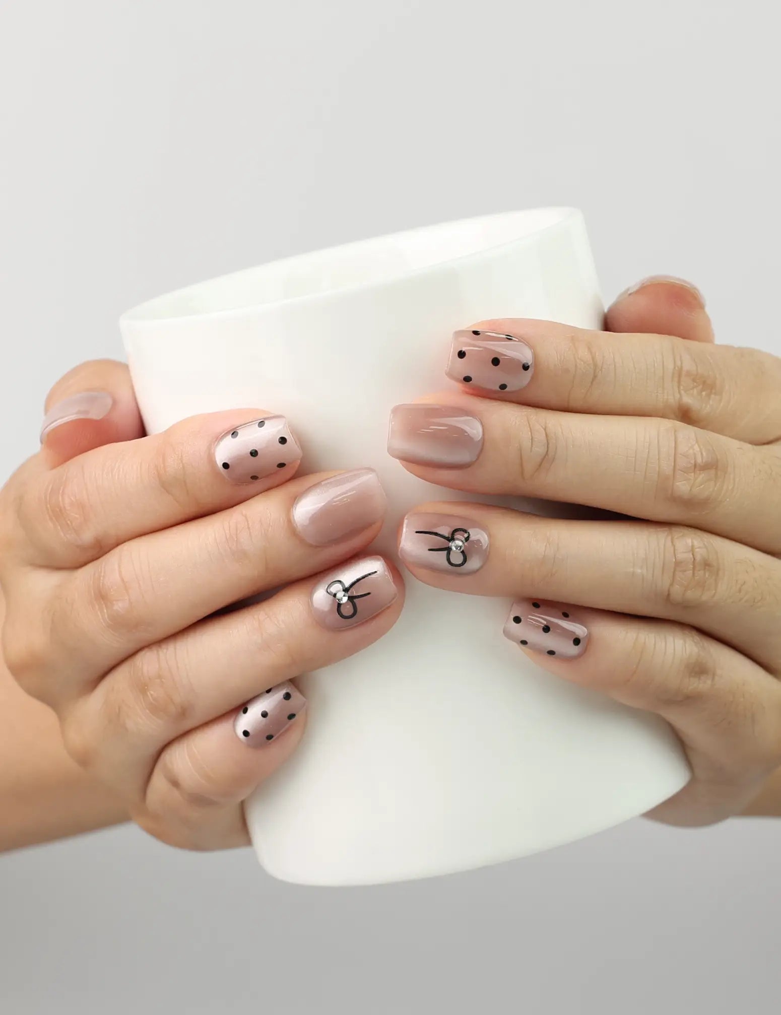 Hand holding a coffee cup while wearing Naillover Mocha Dot Singapore press on nails in taupe with polka dots and bows