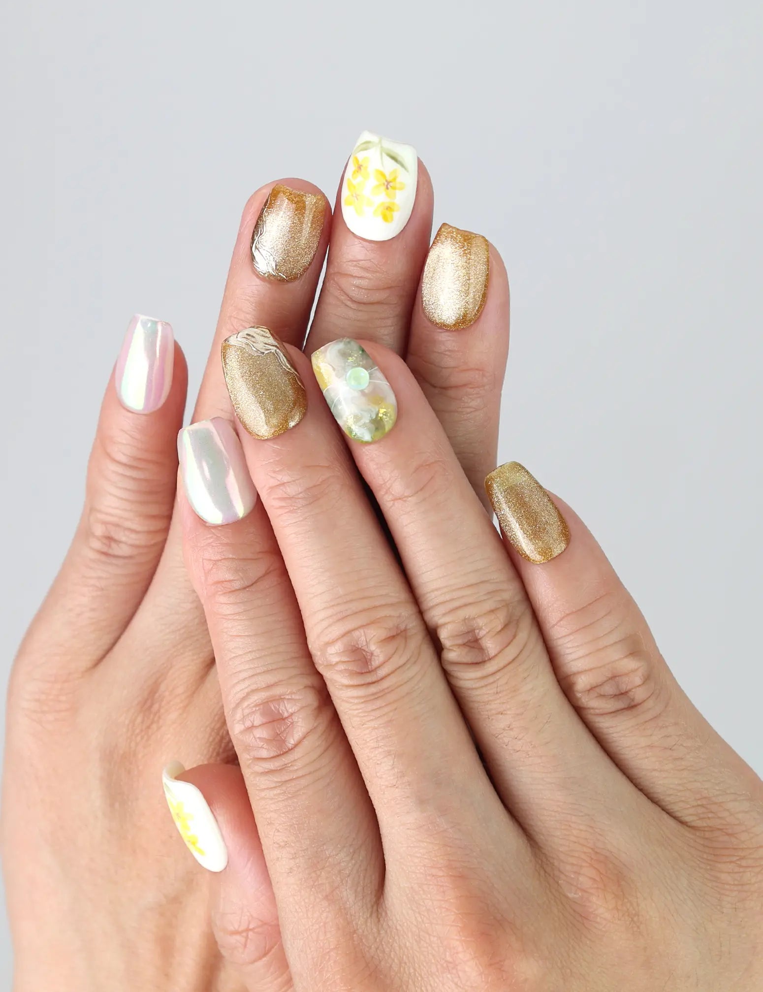Hand wearing Naillover Nature's Glow press on nails with pastel floral prints and gold detailing for a soft, elegant effect.
