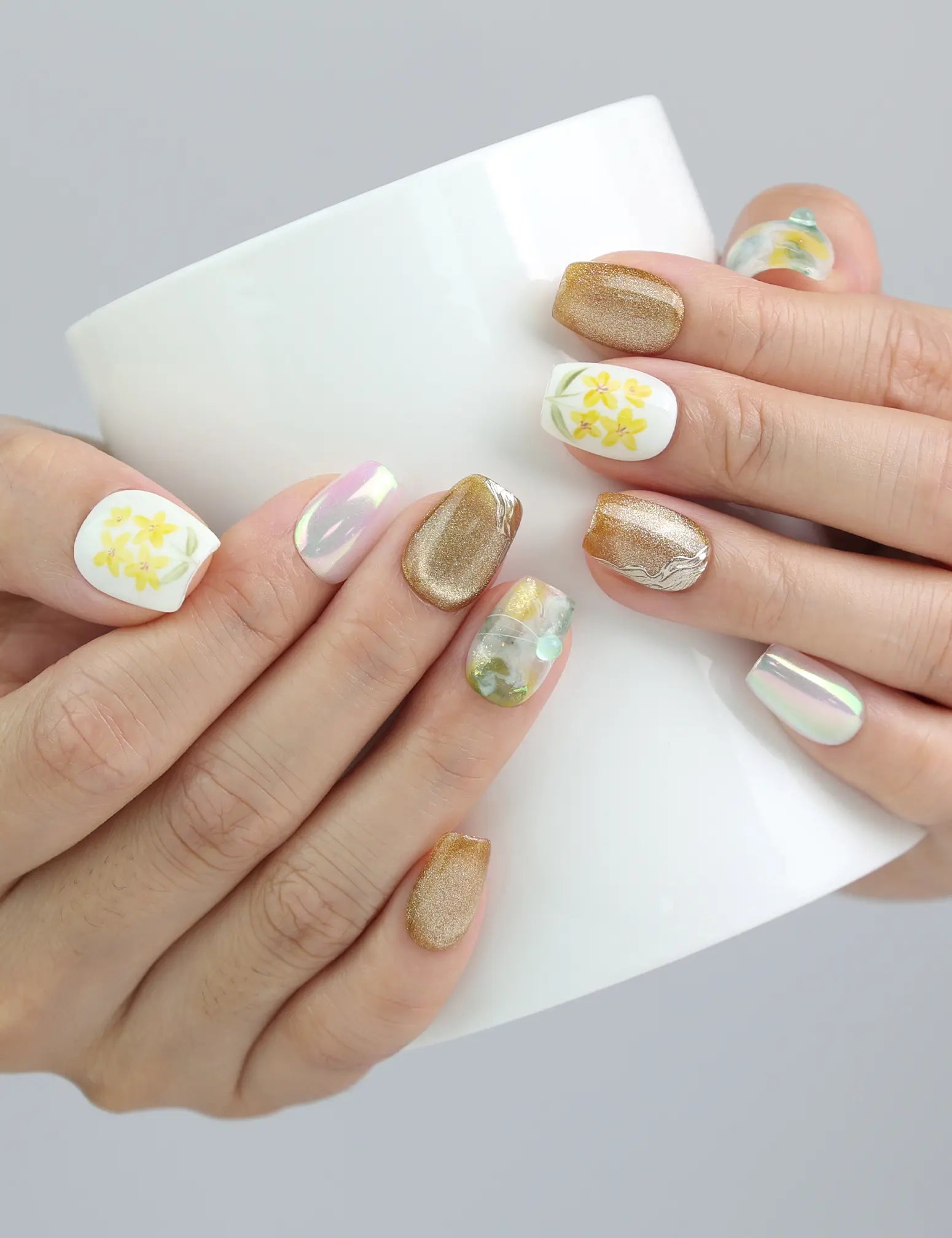 Hand holding a cup while wearing Nature’s Glow press on nails by Naillover, highlighting the balance of floral art and gold shine.