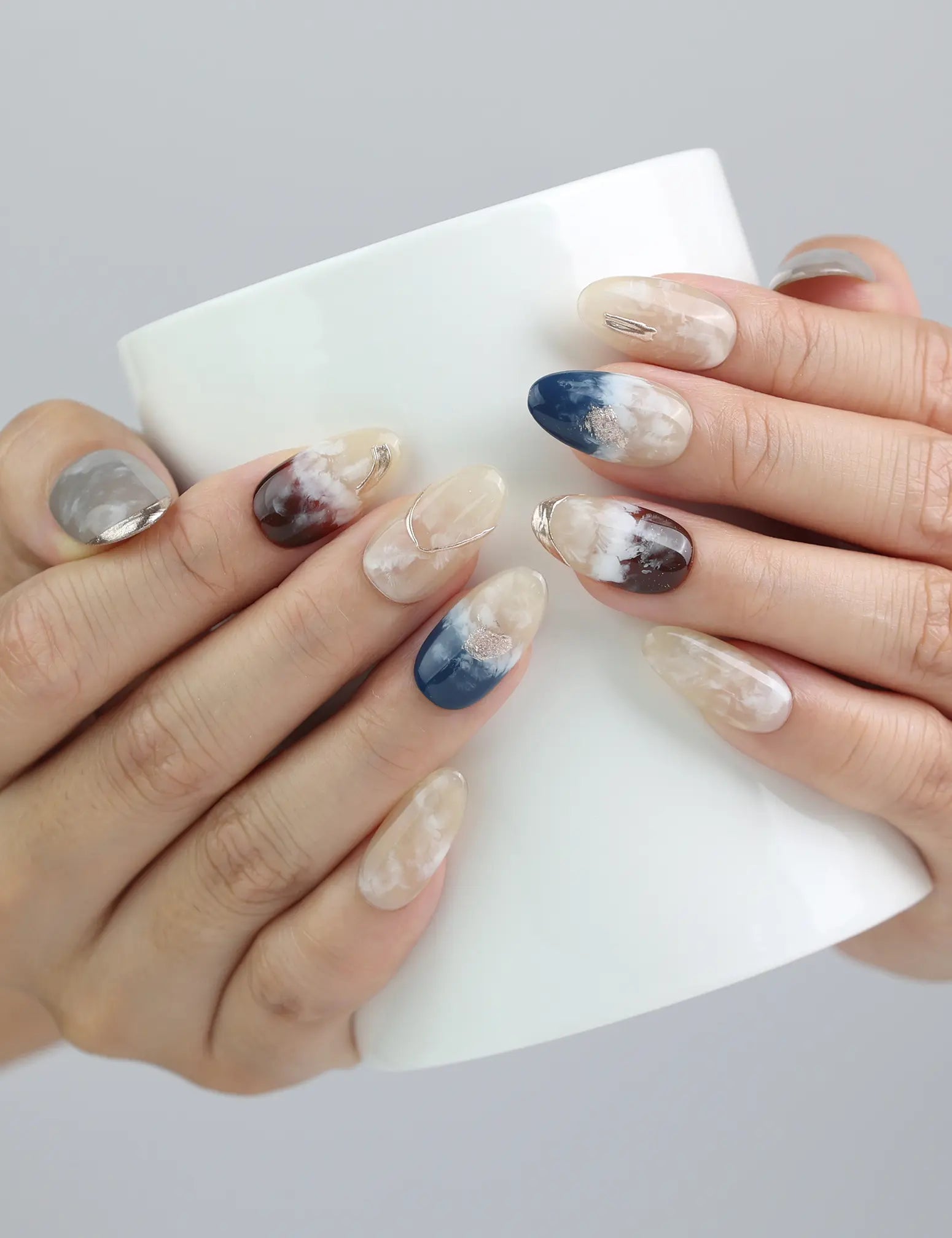 Hand holding a ceramic cup while wearing Oceanic Essence nails, with glimmering blues and subtle marbled effects.