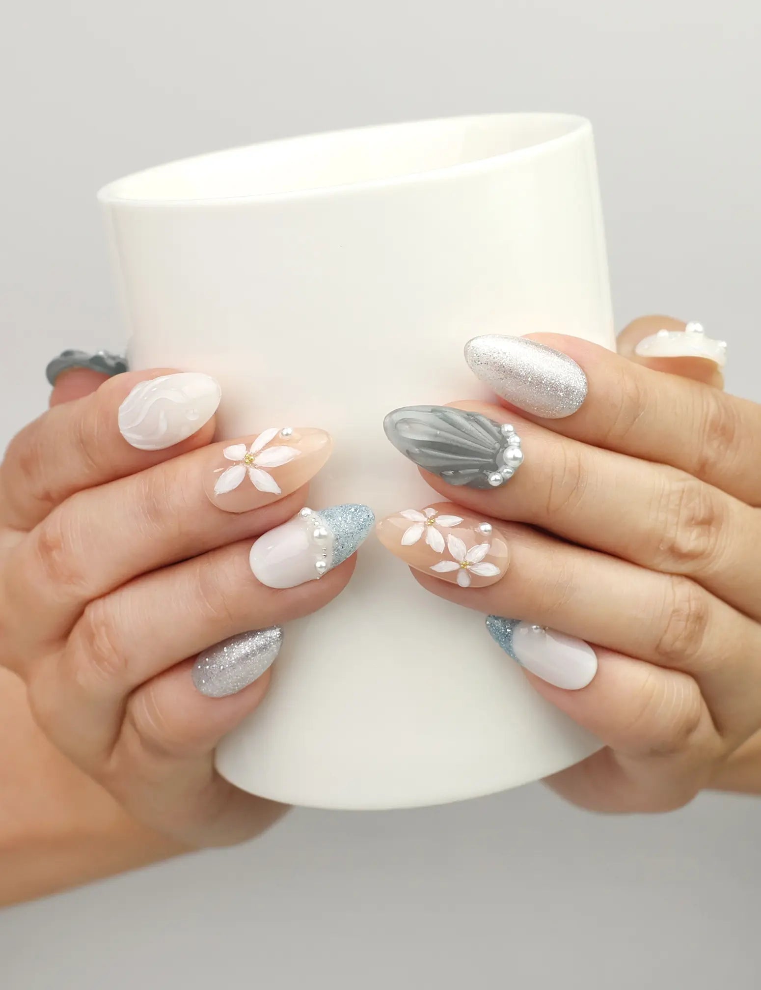 Hand holding a cup wearing Naillover Oceanic Floral Breeze handmade press on nails with floral designs, pearl details, and soft oceanic colors.