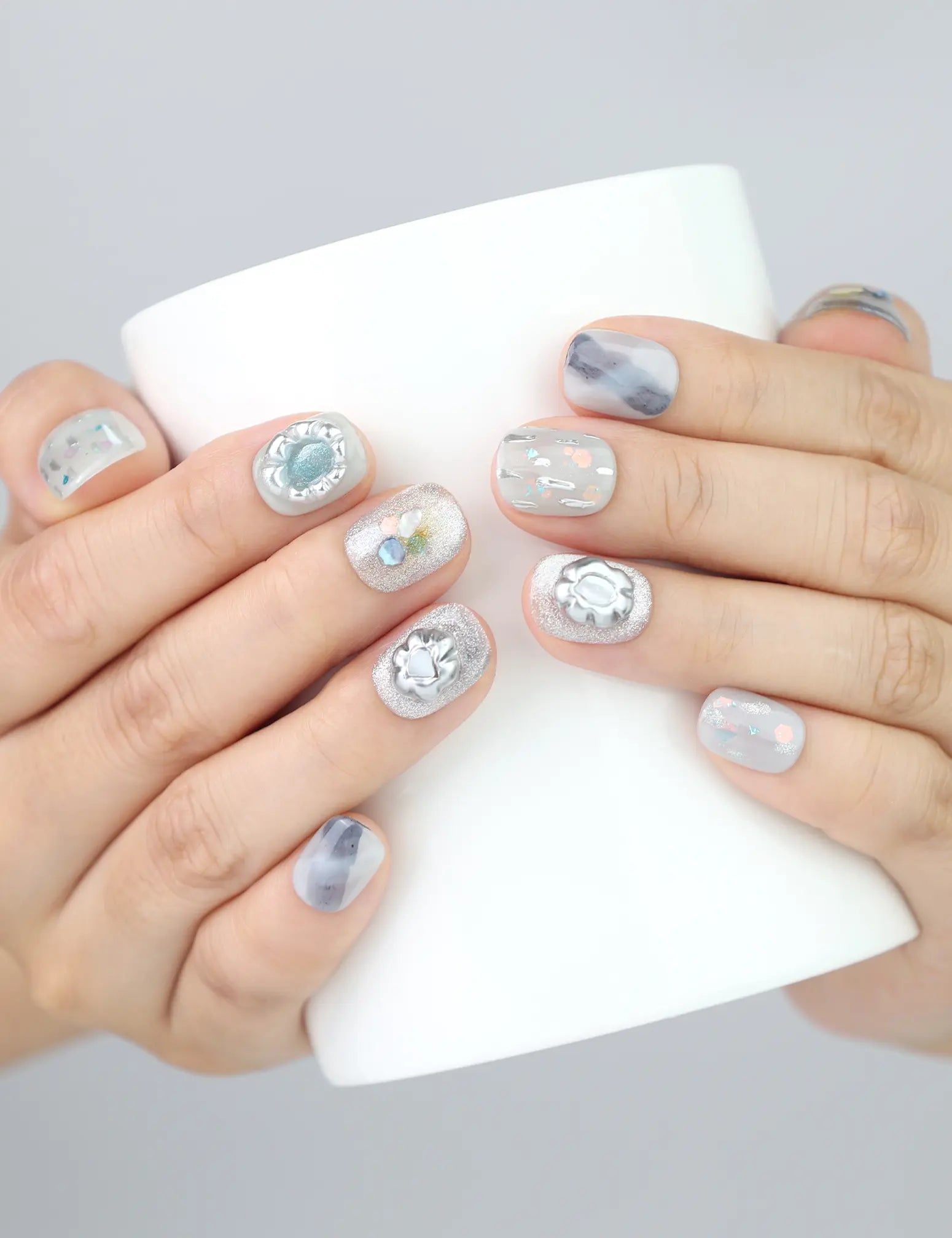 Naillover Opal Whisper nails holding a white mug—showcasing short grey press on nails with glitter accents.
