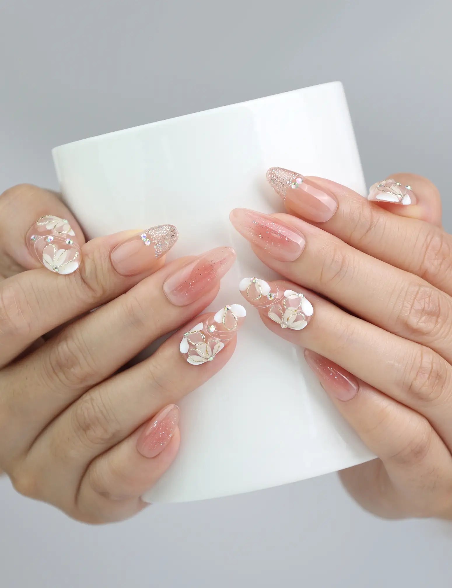 Peachy Glow pink floral press on nails styled on hand holding a coffee cup, showcasing glossy handmade texture