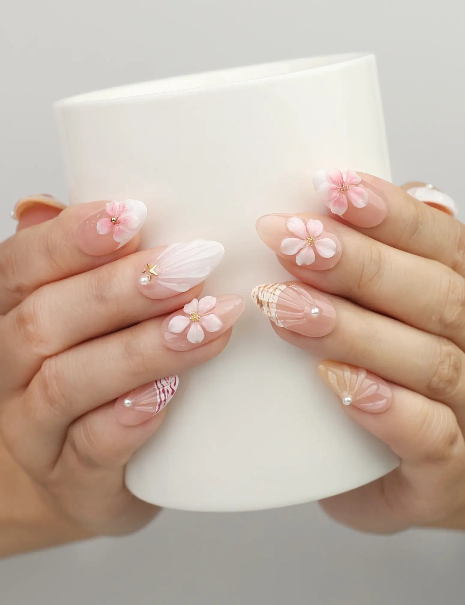 Hand holding a cup wearing Naillover Pink Ocean 3D Floral handmade press on nails with pink flowers, pearls, and shell-like textures.
