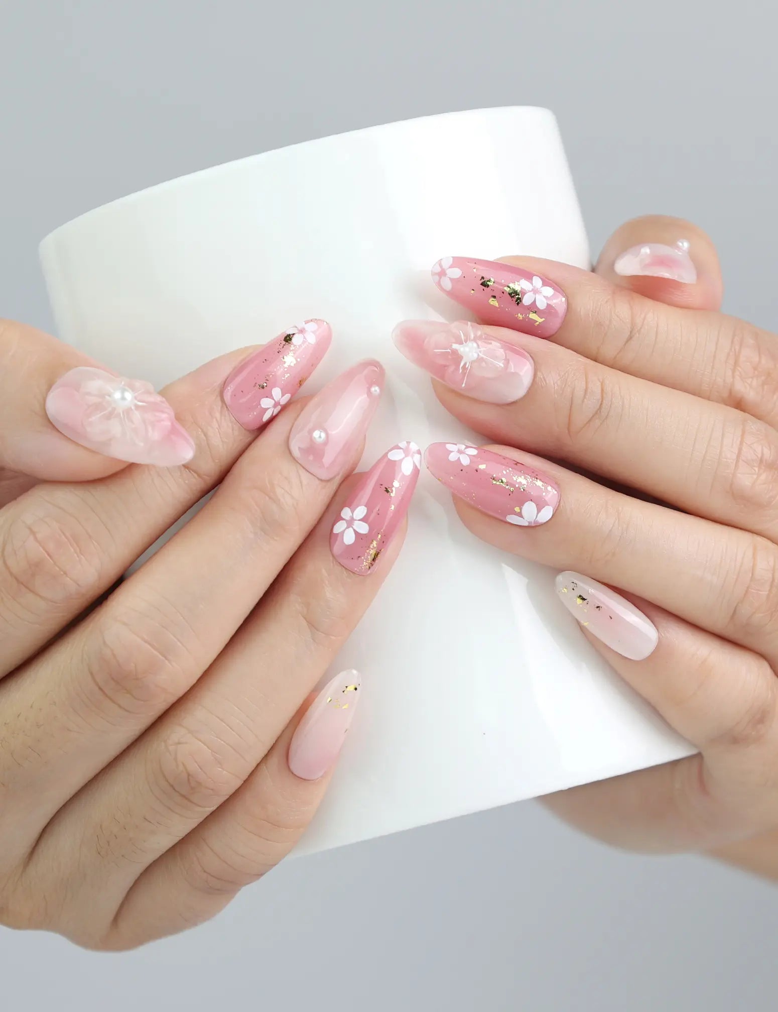 Hand holding a cup with Sakura press on nails, combining soft elegance and whimsical 3D floral design for a cozy spring aesthetic.