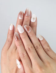 Hand wearing Sandy Shine Singapore press on nails with a soft peach and cream base, accented with gold foil and speckled design.