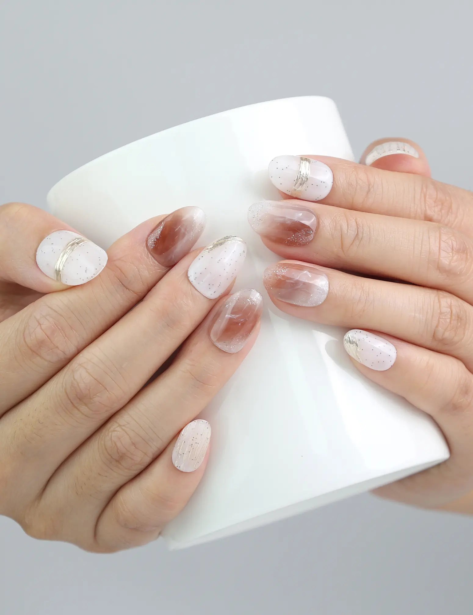 Hand holding a drink while wearing Sandy Shine press on nails, blending casual beach vibes with elegant gold detailing.