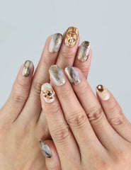 Hand wearing Naillover Seashell Gleam nails, featuring pearl accents and golden foil over creamy white polish.