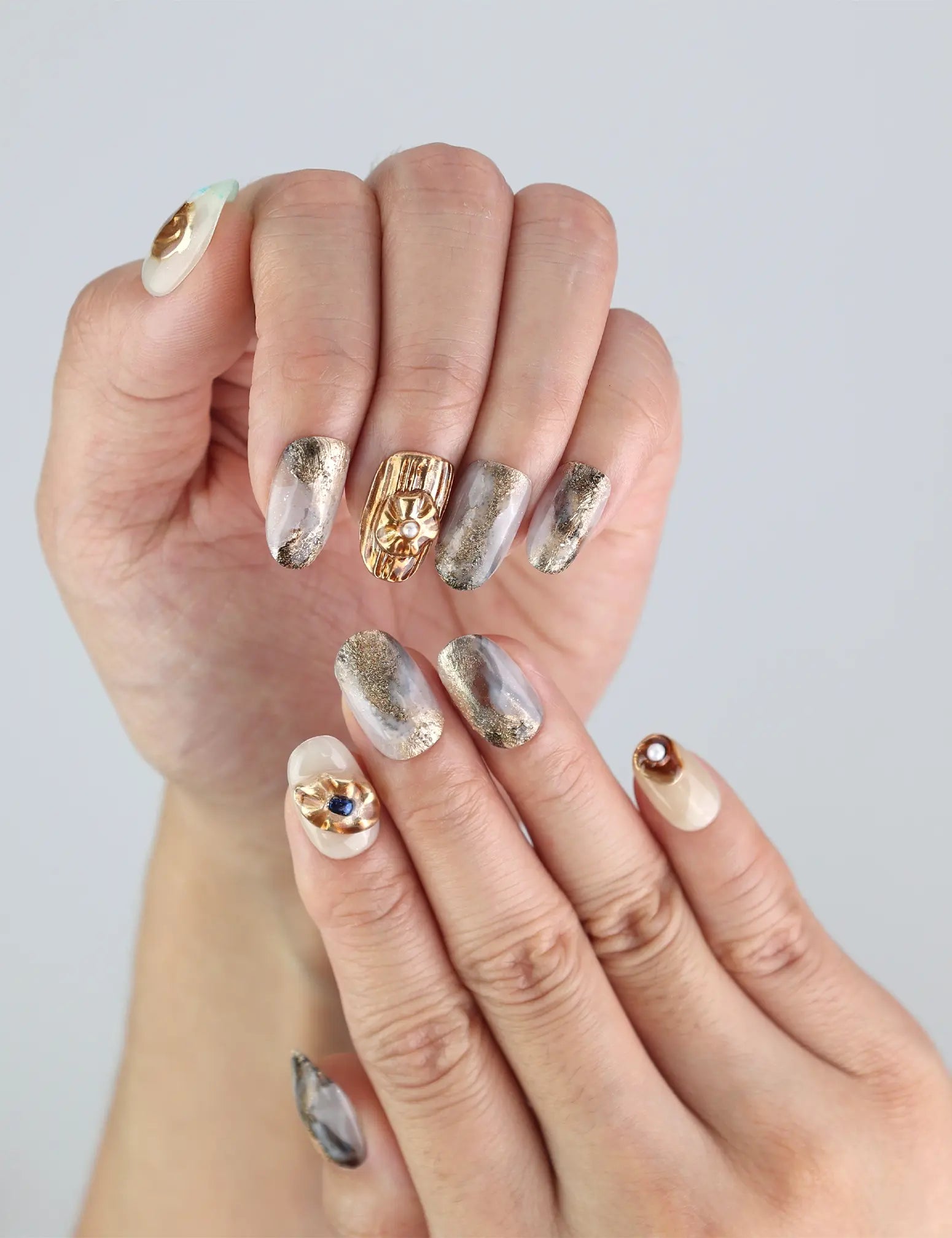 Close-up of Naillover handmade Seashell Gleam press on nails with shimmering gold detail and mini pearl decorations.