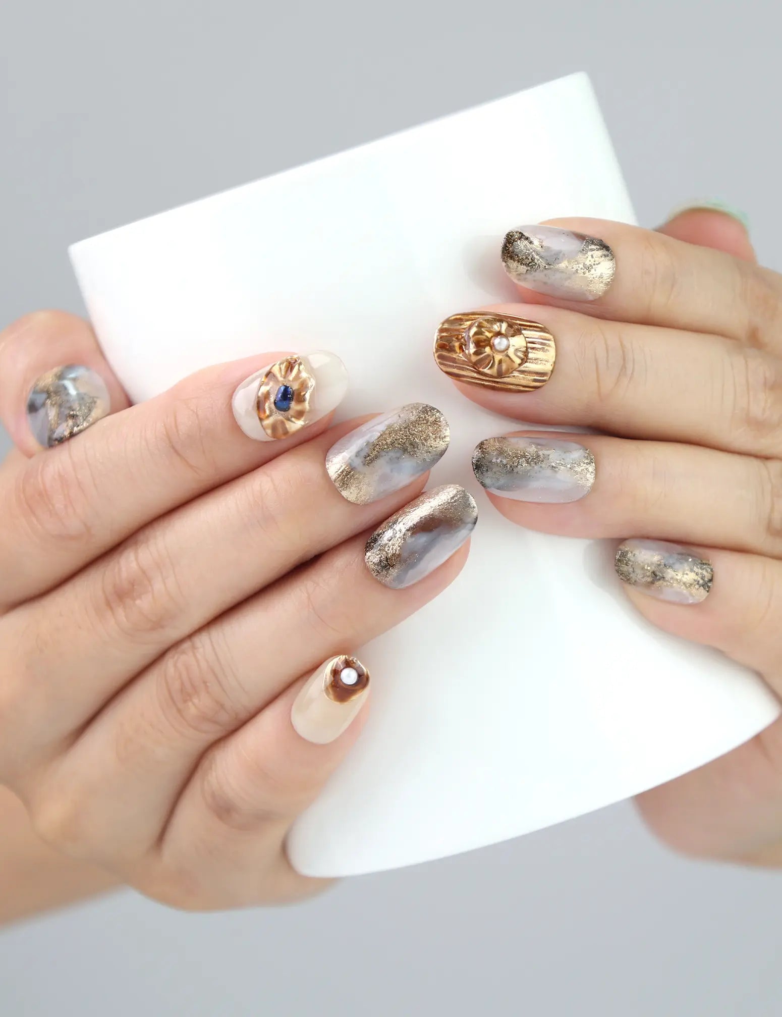 Woman holding a cup while showing Naillover Seashell Gleam nails—creamy tones with gold and pearl detail for an elegant touch.