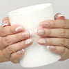 Model holding a cup while wearing Naillover Serene Loops Singapore press on nails with nude tones and pearl accents.