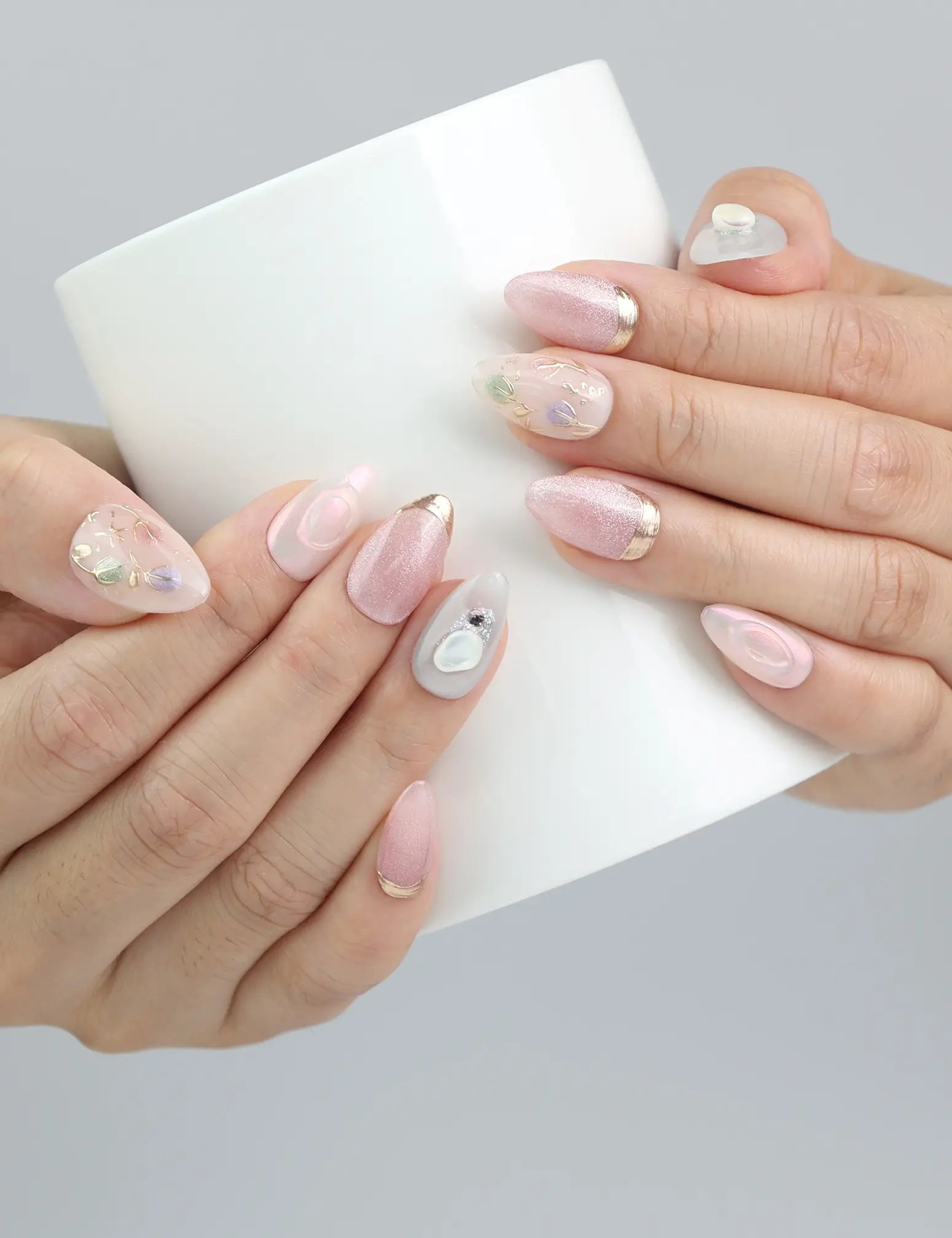 Hand holding a coffee cup with Shimmer Floral pink shimmer press on nails, styled with floral accents.