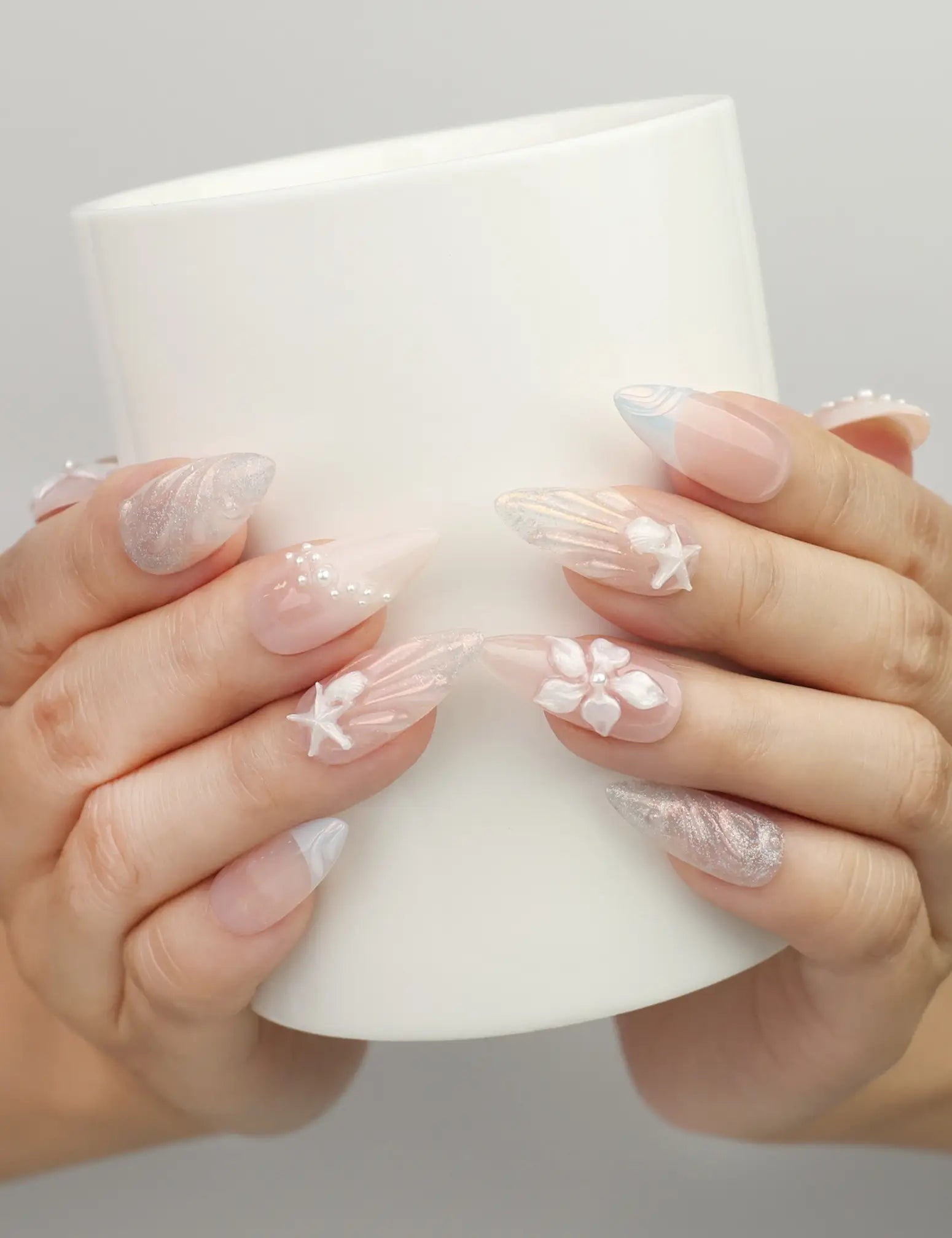 Hand holding a cup wearing Naillover Shimmering Pearl And Floral Elegance handmade press on nails with pearls and blue floral details.