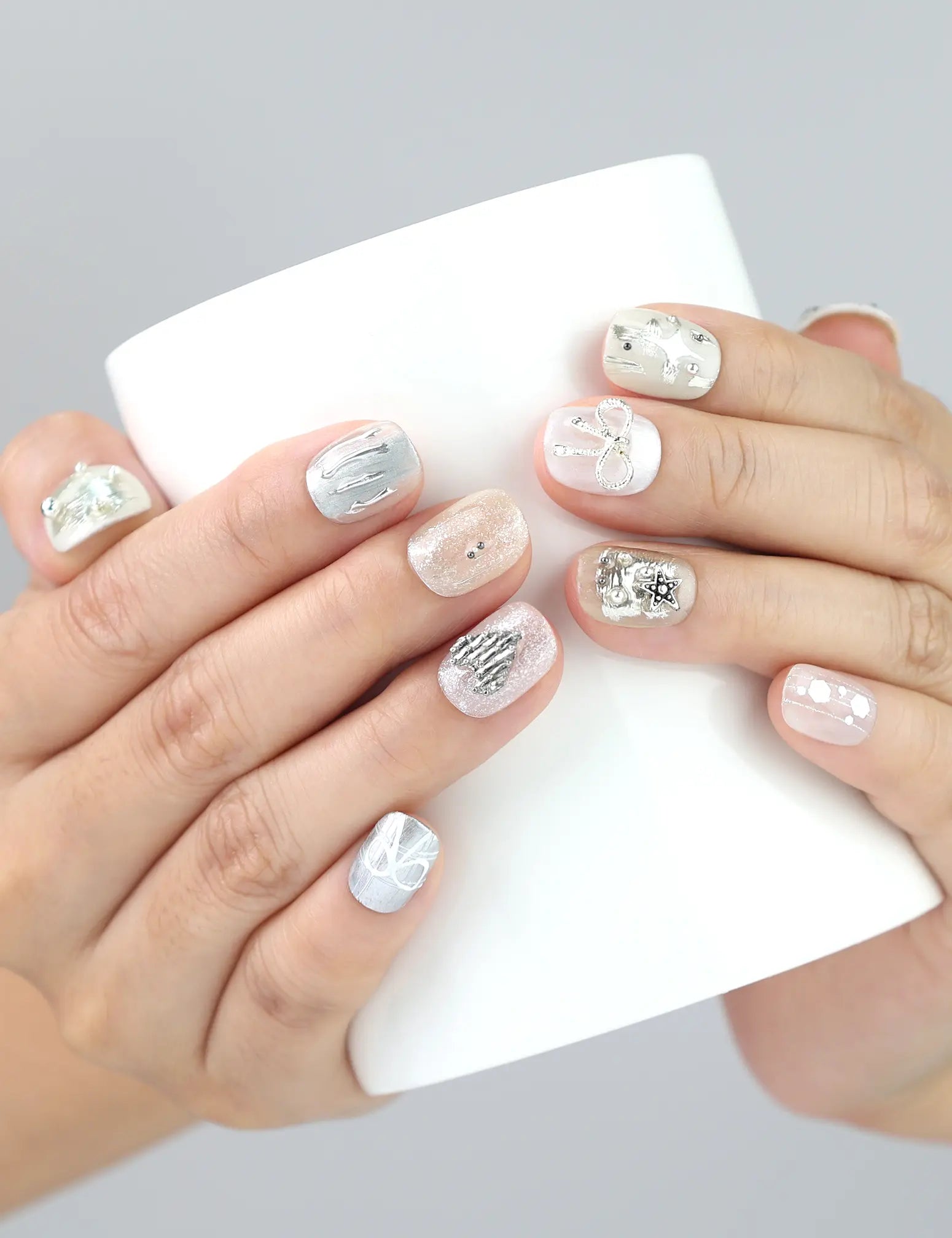 Hand holding a cup while wearing Naillover Silver Bow handmade press on nails—white short nails with silver bow and stud embellishments.