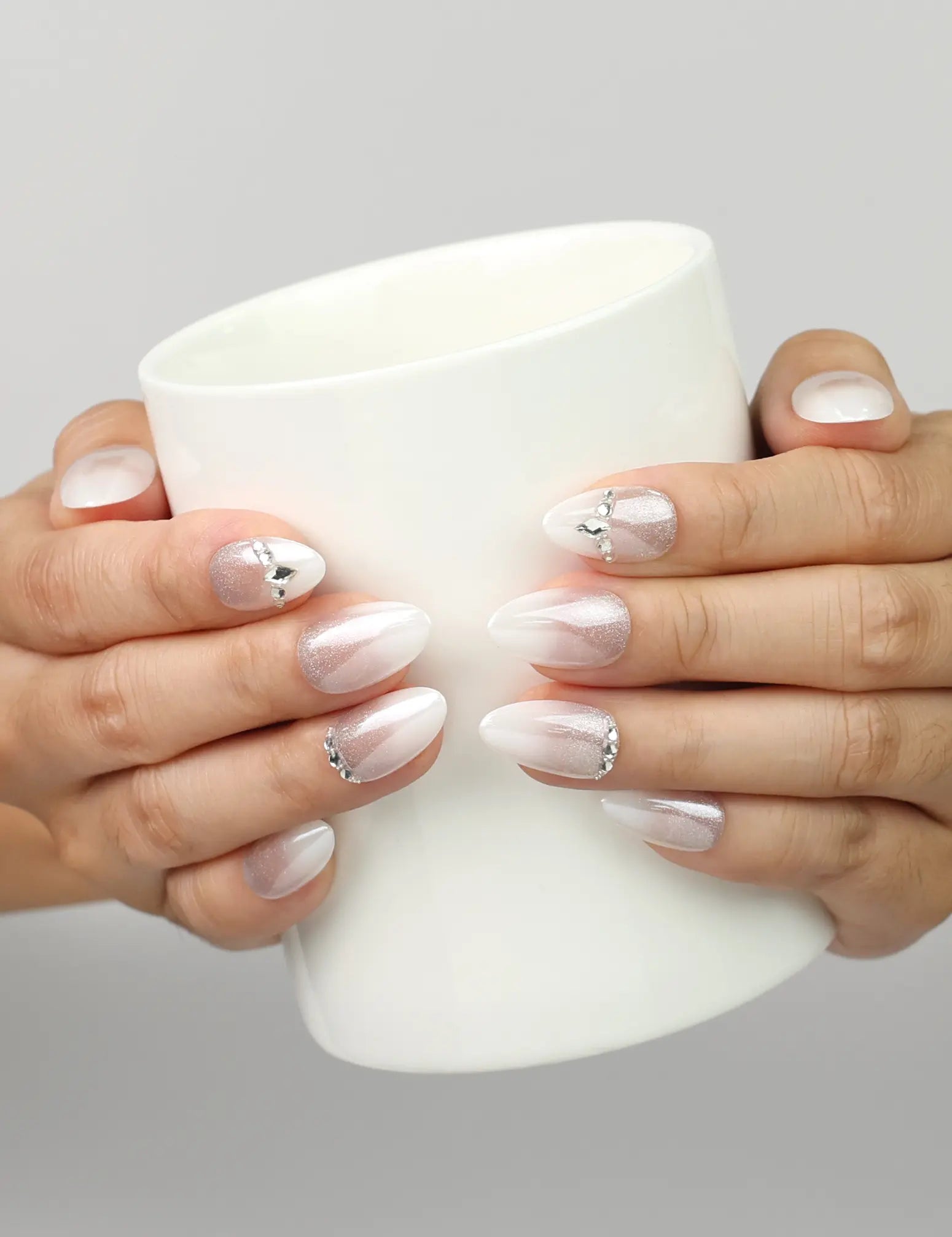 Model holding a cup while wearing Naillover Silver Gleam handmade press on nails with white base and rhinestone accents.