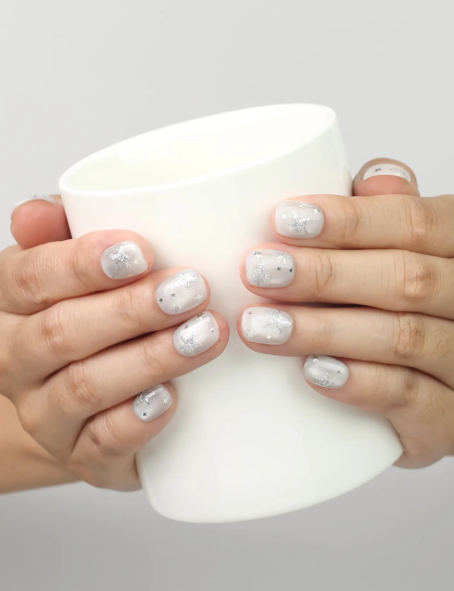 Model holding a cup while wearing Naillover Silver Skies handmade Singapore press on nails with shimmering silver stars.