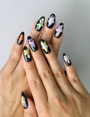 Hand model wearing almond-shaped press-on nails with glossy black base and detailed purple iris flower design
