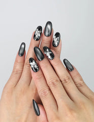 Hand model wearing black oval-shaped press-on nails with silver ombré fade and 3D butterfly crystal charms