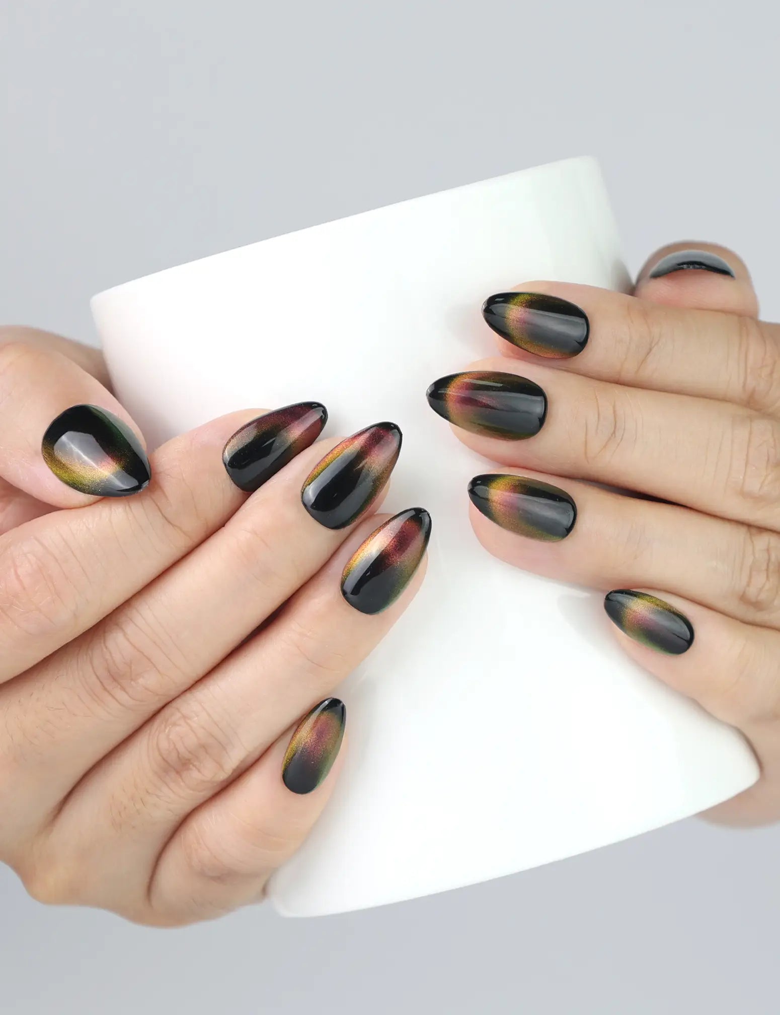 Hand holding coffee cup while wearing Noir Fade Tips black cat eye press-on nails with French fade from naillover.
