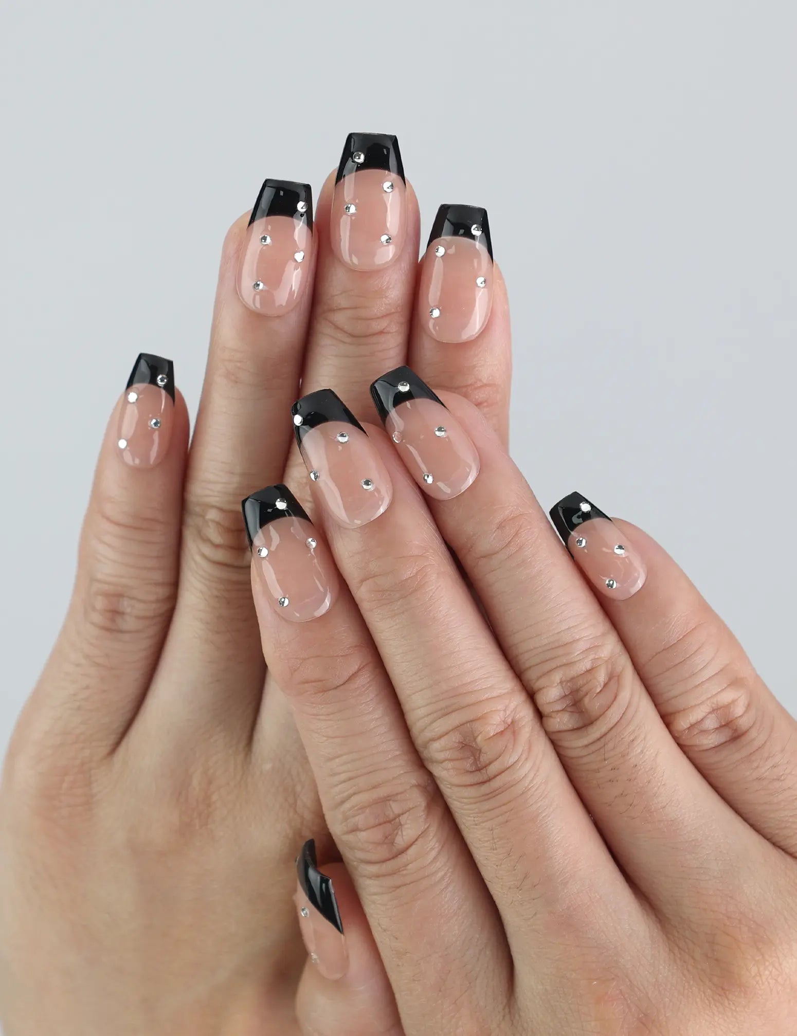 Close-up of hand wearing Naillover Nude Edge press on nails with black French tips and glossy nude gradient finish.