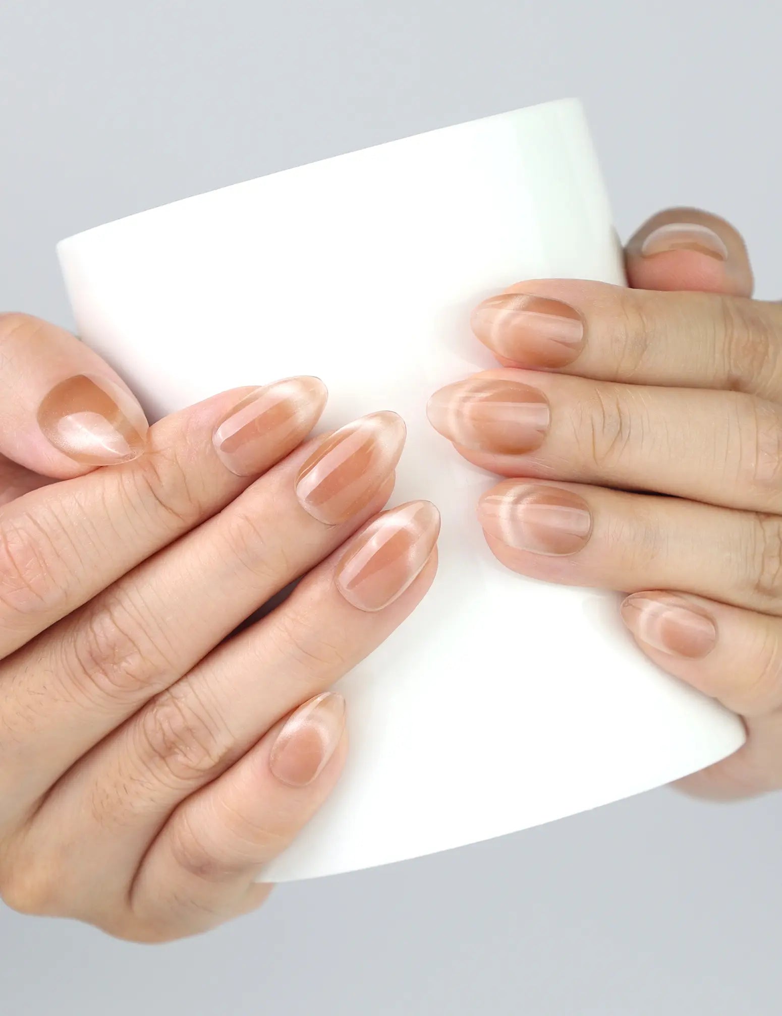 Hand holding ceramic mug with Nude Fade Tips press on nails by Naillover, soft neutral vibe.