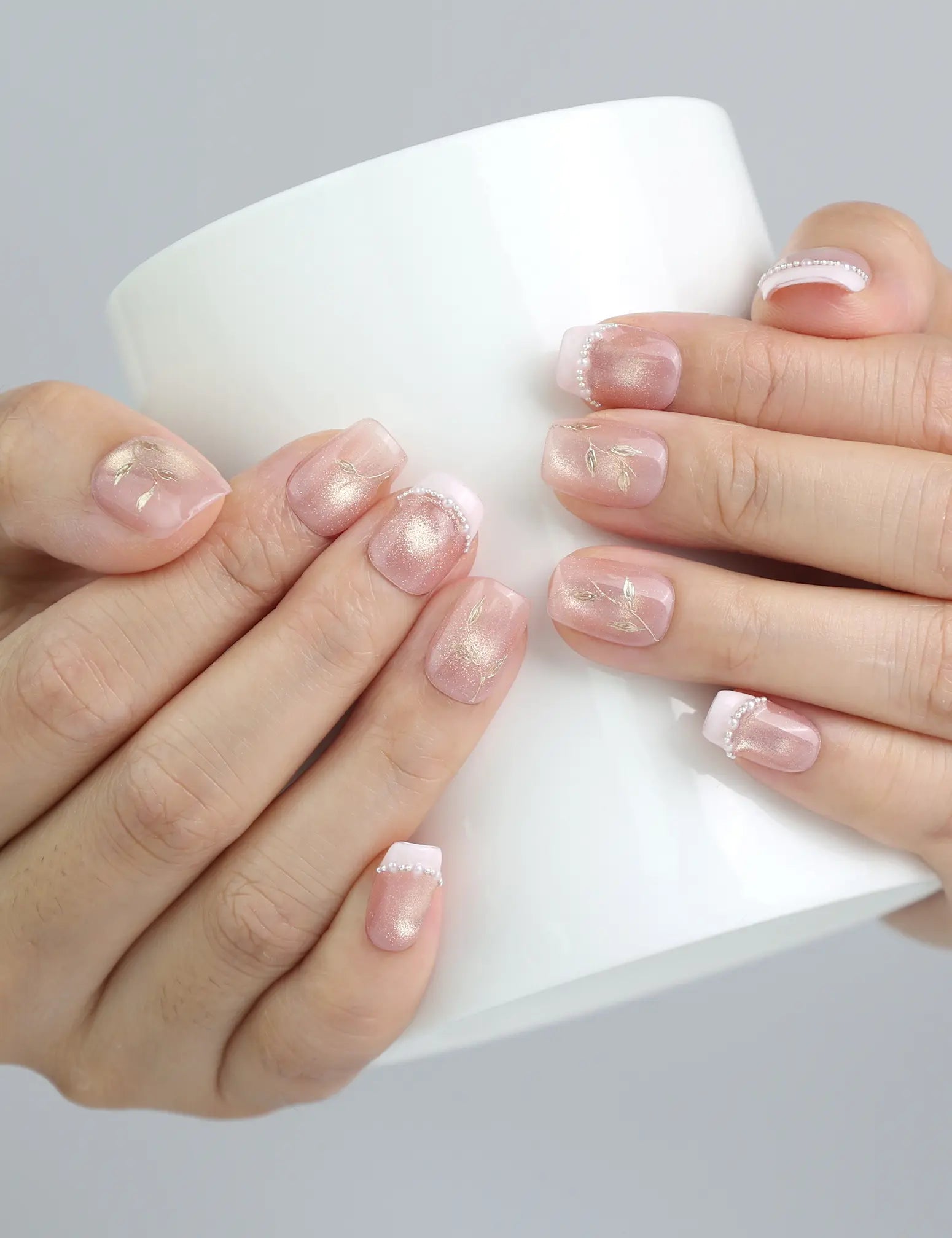 Holding a cup with peach-toned press on nails featuring gold details and subtle glitter, handmade by Naillover in Singapore