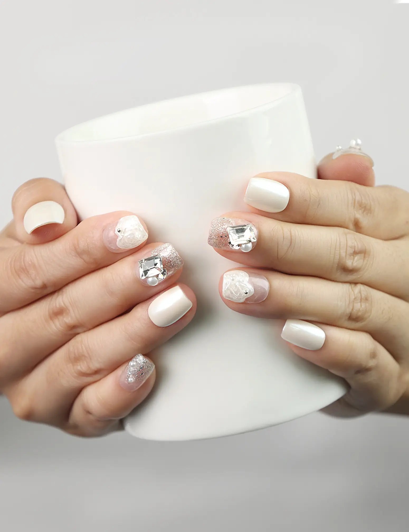 Hand holding a cup wearing Pearl Sparkle white press-on nails with pearls and silver gemstones, Singapore handmade nails by naillover
