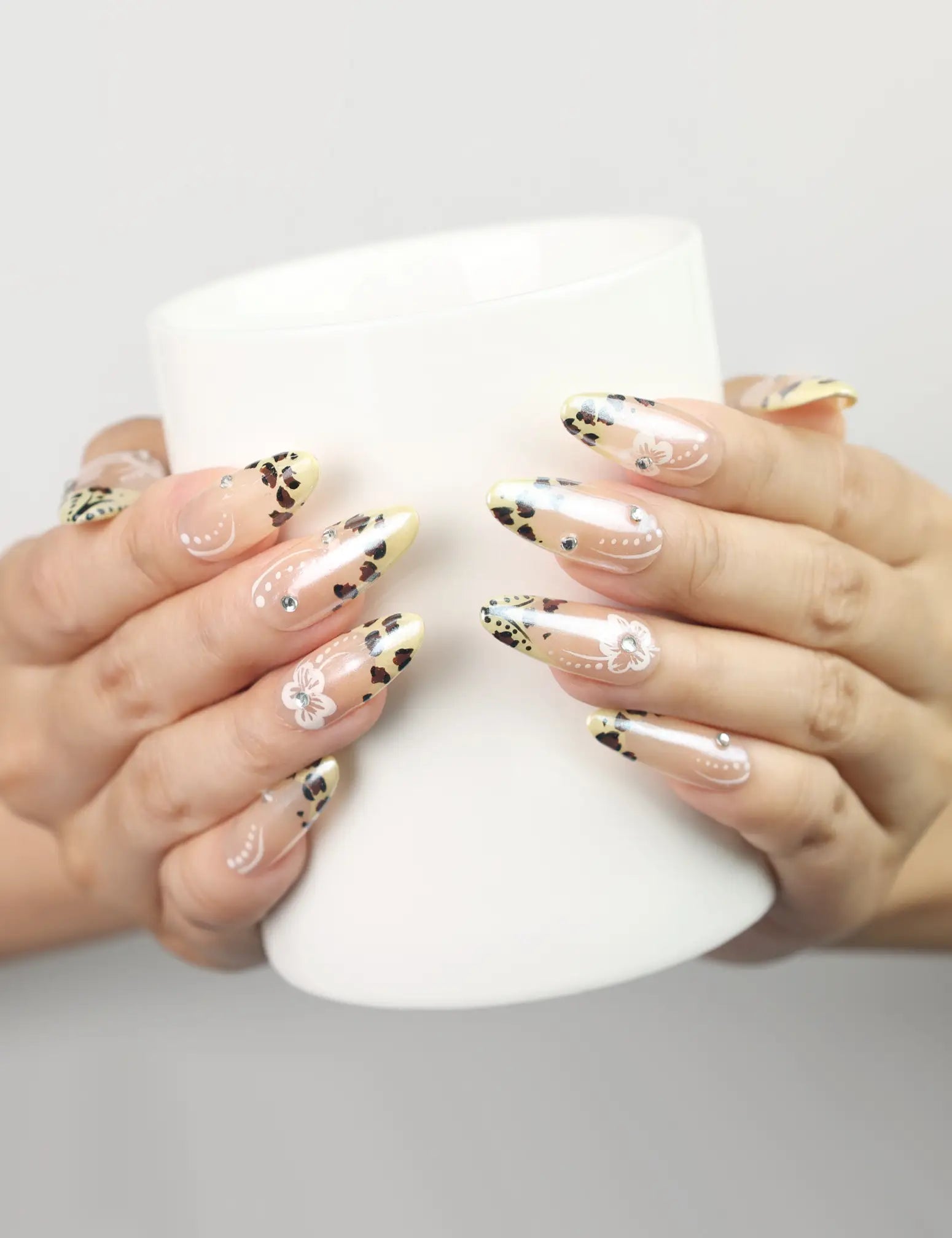 Hand holding coffee cup while wearing Pearly Blossom Singapore press on nails with leopard print and floral designs