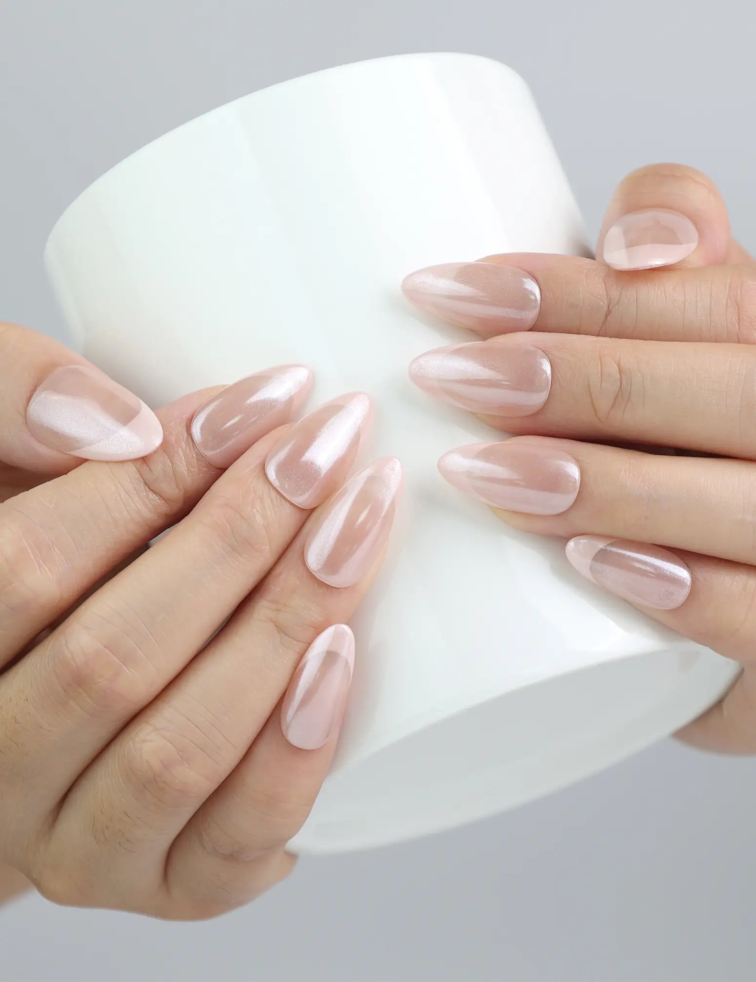 Hand holding a cup, showcasing Naillover’s pink almond press-on nails in a delicate rose petal tone and glossy finish
