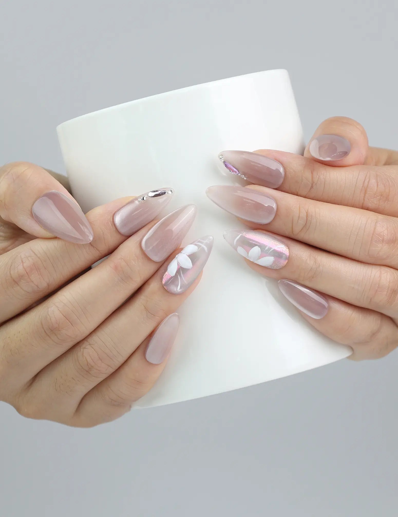 Hand holding a cup, showcasing Naillover’s pastel almond nails with feminine white floral details