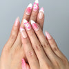 Hand model wearing almond-shaped press-on nails with layered pink 3D flowers in soft pastel and bold fuchsia tones