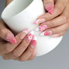 Hand holding a cup, showcasing Naillover’s pink floral press-on nails with pastel and fuchsia 3D petals