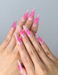 Hand model wearing pink almond press-on nails with holographic ombré glow and delicate heart details