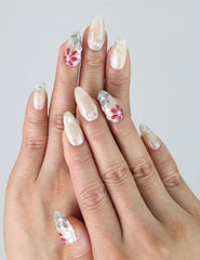 Hand model wearing almond-shaped press-on nails with red, white, and grey 3D floral accents
