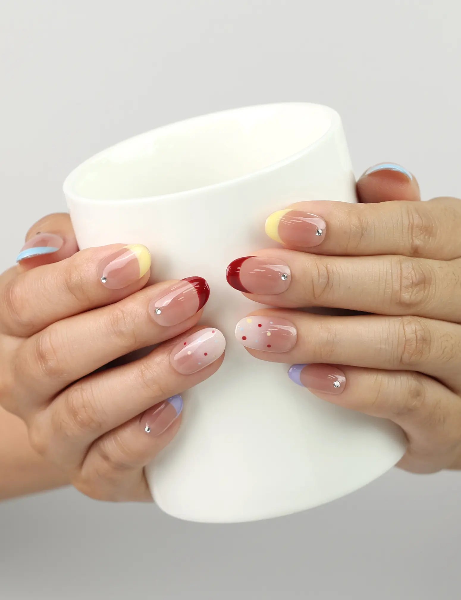 Hand holding a cup with Rainbow Tips handmade press on nails, blue, yellow, and red glitter tips adding a fun and lively accent.