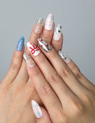 Hand model wearing almond-shaped press-on nails with red bows, black-and-white checkered tips, and gem accents