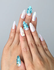 Hand model wearing blue almond-shaped press-on nails with raised seashell patterns and metallic starfish accents