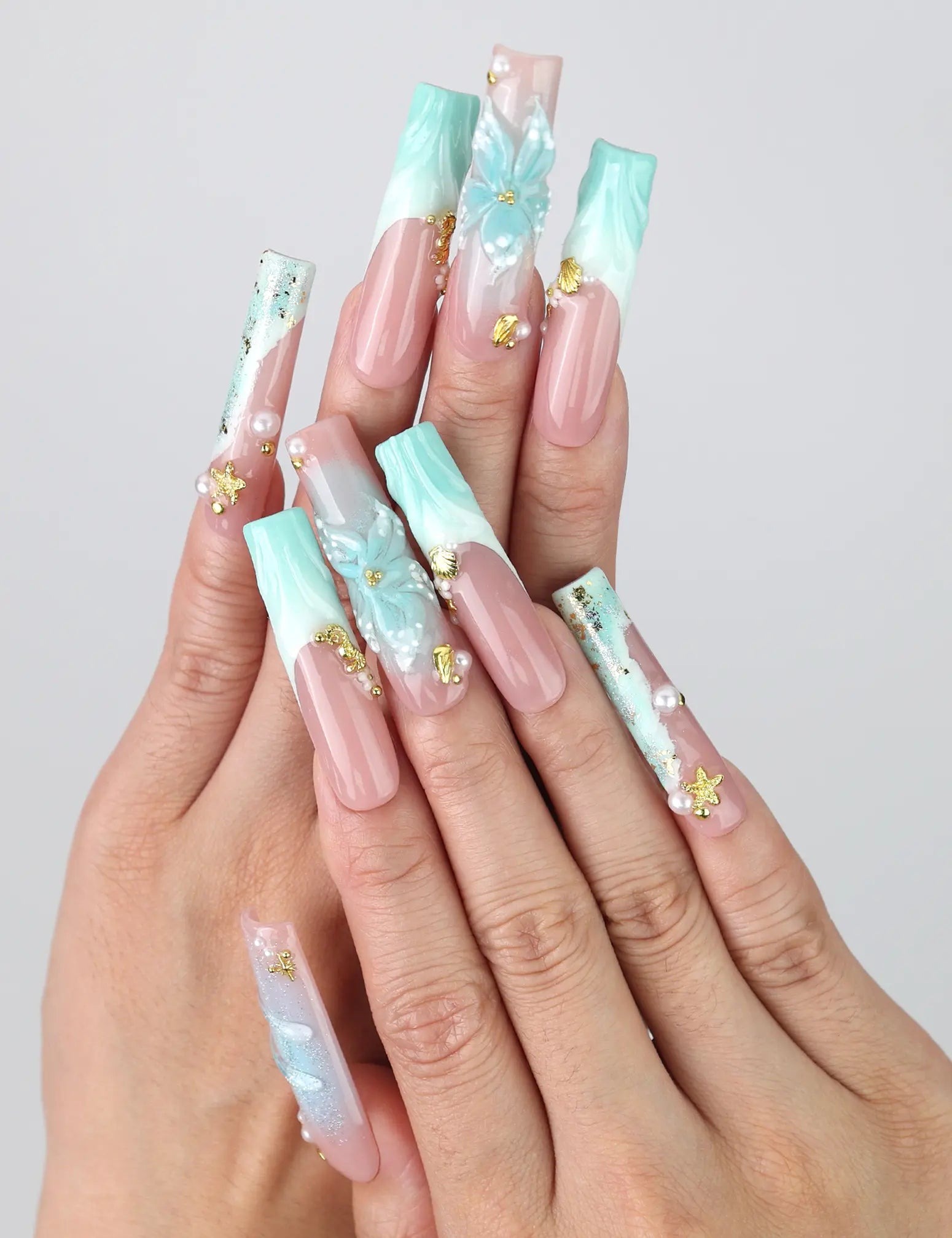 Hand gesture showcasing Singapore handmade long pipe press on nails with 3D floral art, ocean wave designs, and gold starfish accents by Naillover