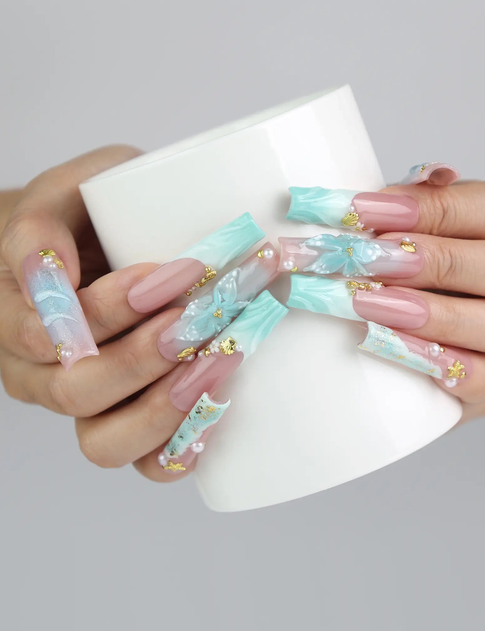 Hand holding a cup while wearing tropical ocean-themed long pipe press on nails with 3D elements and gold accents by Naillover