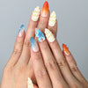 Hand model wearing almond-shaped press-on nails with ocean-inspired colors and raised seashell charms