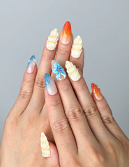Hand model wearing almond-shaped press-on nails with ocean-inspired colors and raised seashell charms