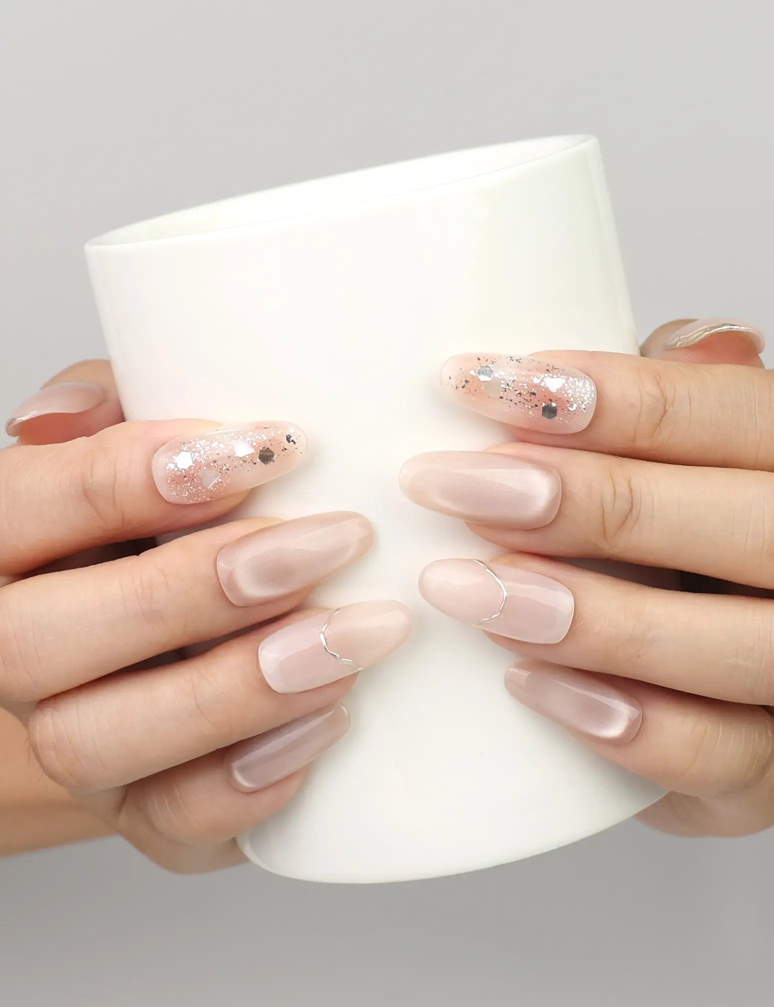 Hand holding a cup while wearing Naillover Shimmering Beige handmade press on nails with elegant cat eye effect and gold foil highlights.