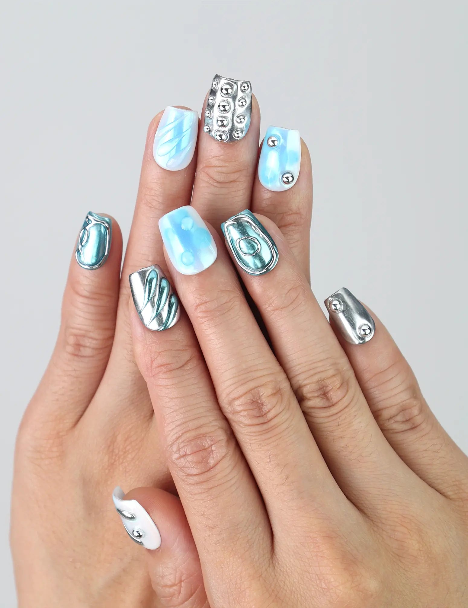 Hand model showing short coffin-shaped blue press-on nails with glossy metallic silver and 3D water droplet textures